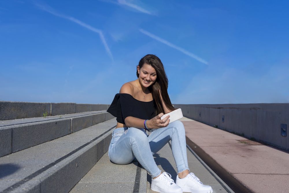 One woman with long hair sitting on staircase while using mobile phone with a big smile
