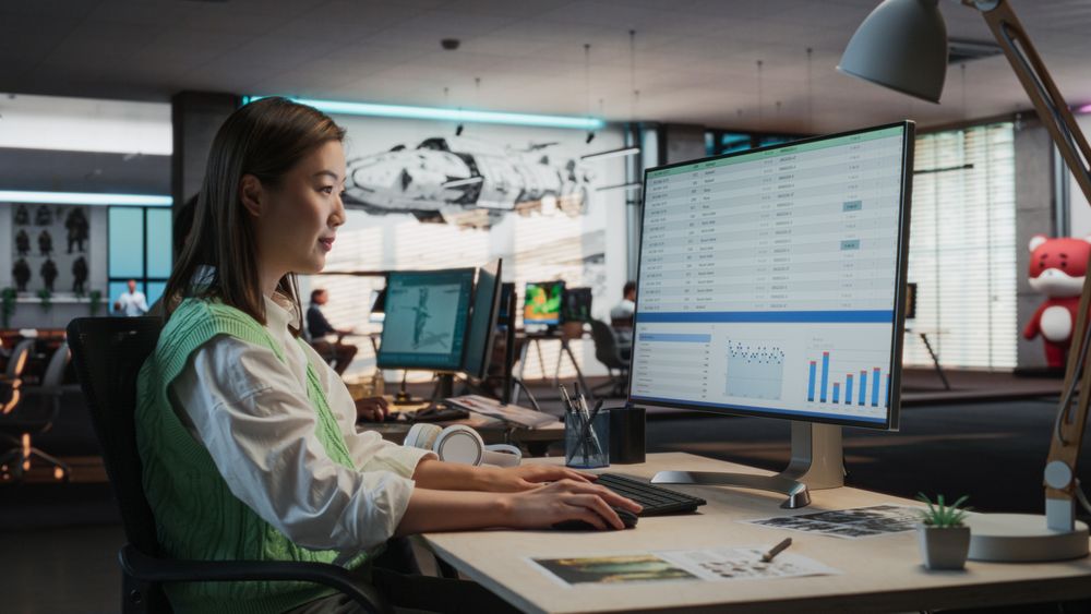 Female Asian Manager Working on Desktop Computer With Analytics Reporting Software on Display in Office.