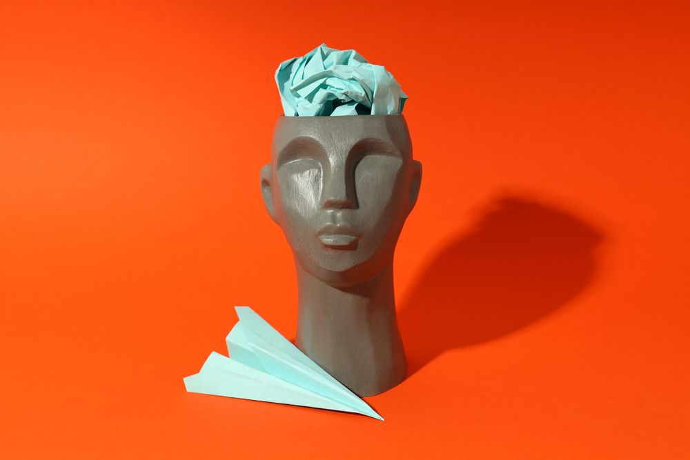 Grey bust of head on red background with paper airplane