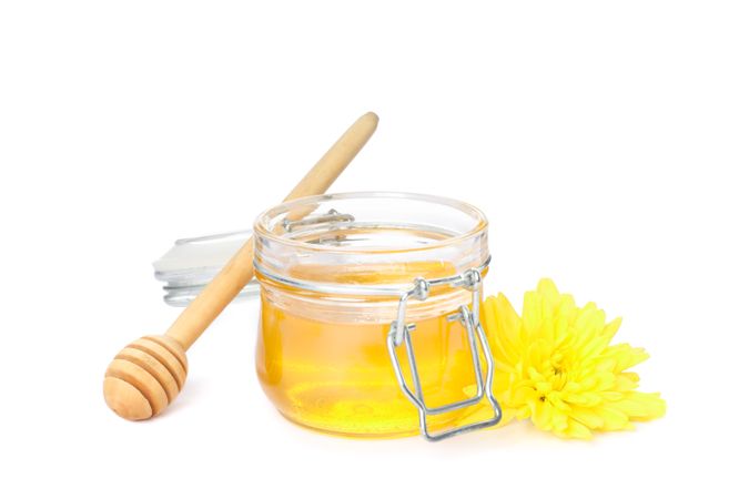 Dipper, chrysanthemum and glass jar with honey isolated on studio background