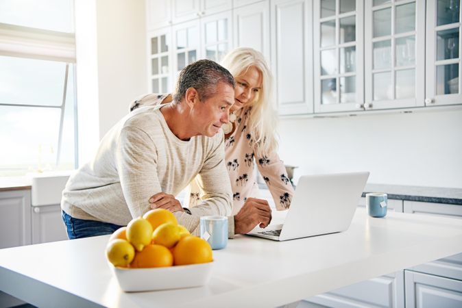 Older couple leaning over a laptop on the kitchen counter