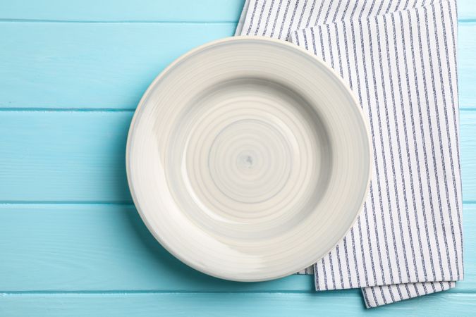 Kitchen towel with plate on wooden background, top view