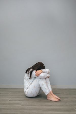 Woman crying in grey room with head hidden