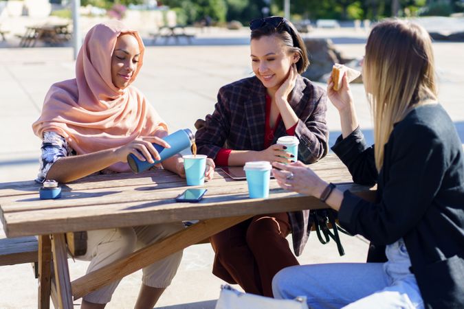 Happy Muslim woman in hijab, pouring coffee from insulated mug into disposable cup