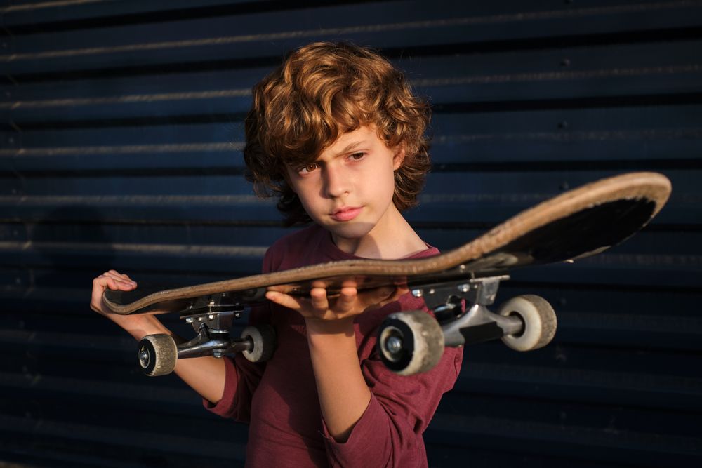 Boy examining skateboard against blue wall