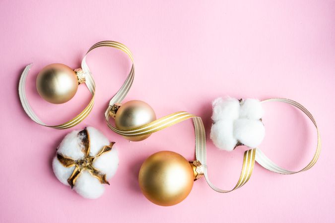 Gold Christmas baubles and cotton on pink background