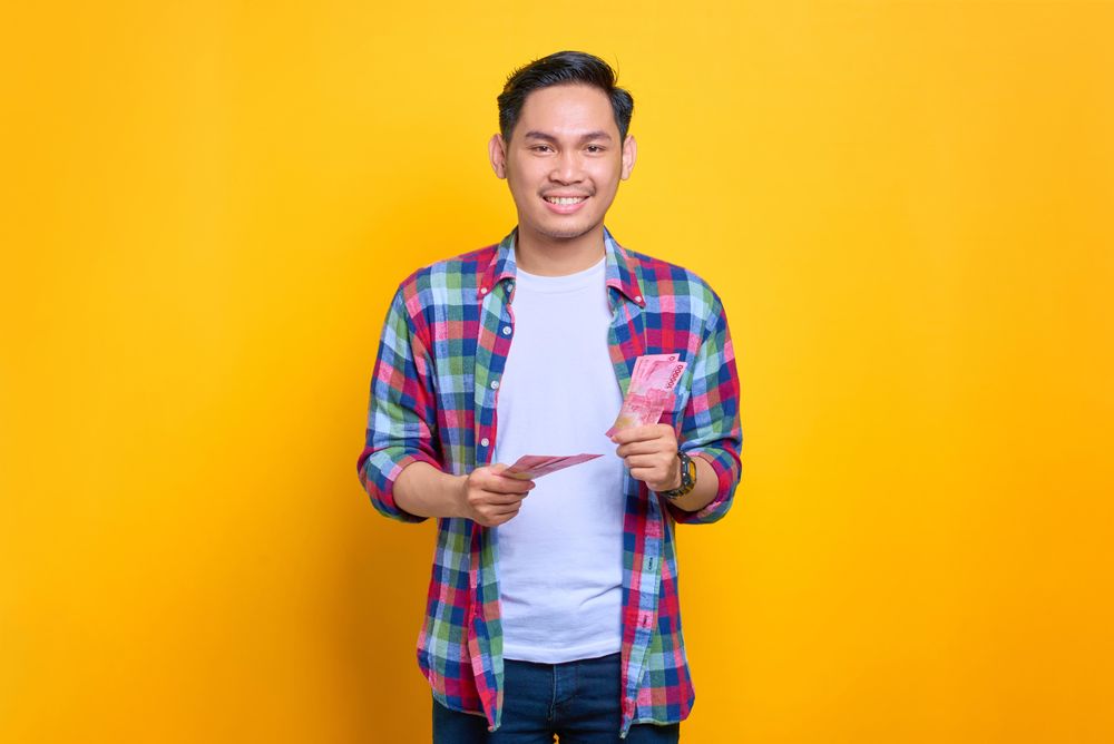 Smiling Asian man with cash in both hands in studio shoot