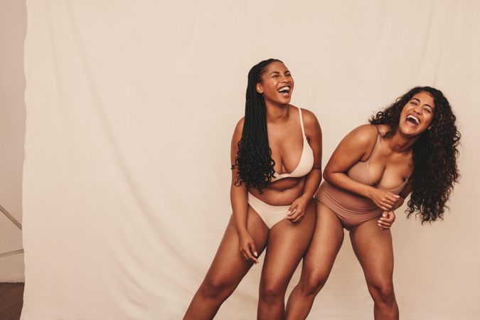 Female friends dancing cheerfully while wearing underwear in studio model shoot