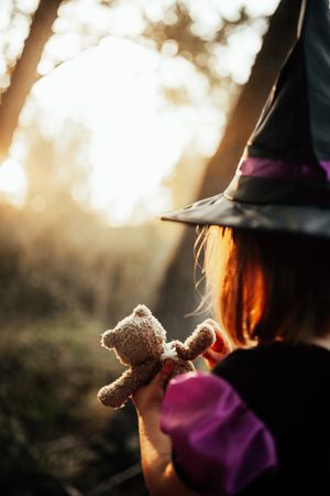 Back of girl with teddy bear in witches costume, vertical
