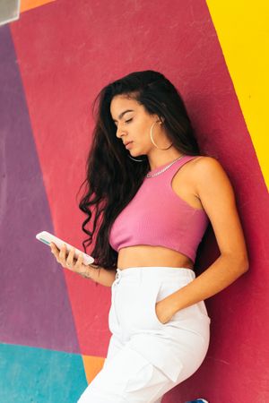 Latina woman using smartphone leaning on a colorful wall