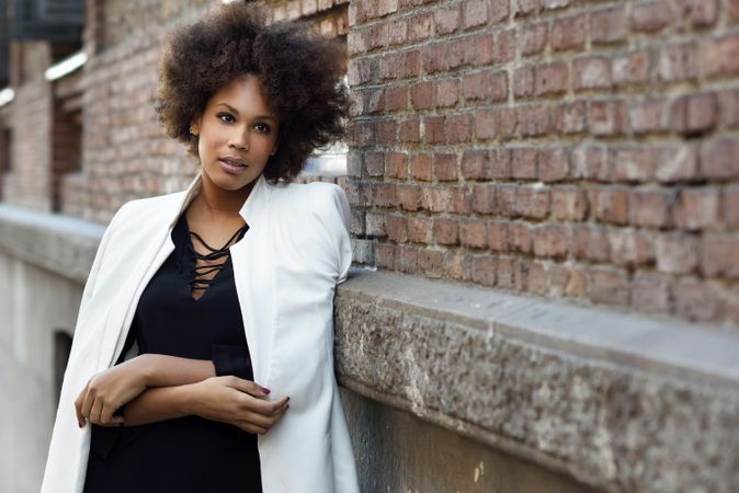 Female in dress with blazer draped over shoulders standing next to outdoor wall