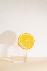 Glass of water with orange slide on neutral background