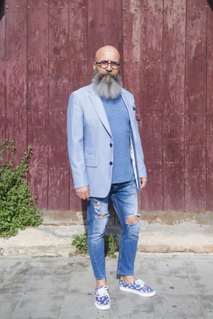 Front view of a mature trendy bearded hipster standing against a vintage red door outdoors while looking to camera