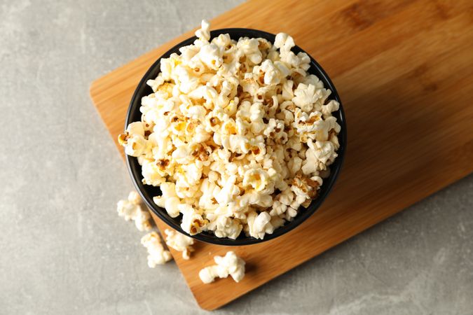 Bowl with popcorn and board on grey background, copy space