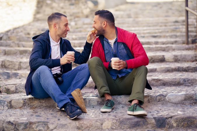 Two men sharing food while sitting outside with to go coffee