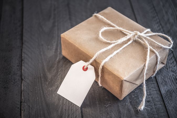 Paper-wrapped gift with empty tag on rustic table