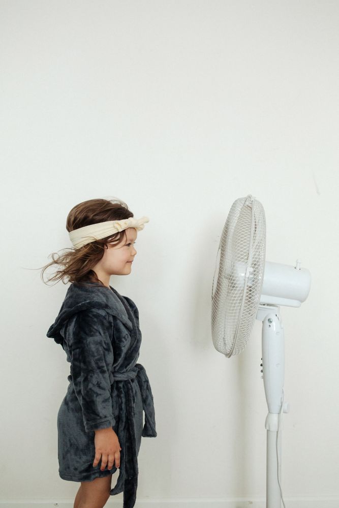 Little girl standing against fan at home