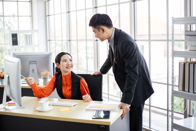 Asian male and female colleague discussing work in bright office