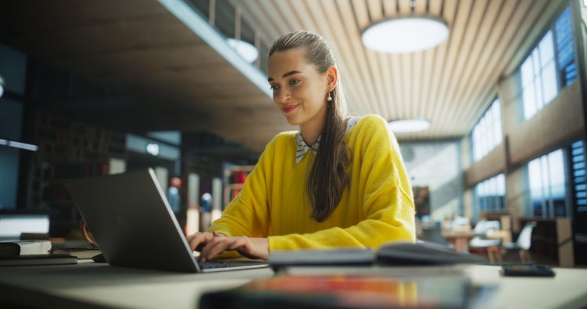 Thoughtful Multiethnic College Student Using Laptop Computer to Study in a Public Library. Beautiful Young Woman Learning Online, Getting Ready for Exams, Browsing Internet to Prepare for Class