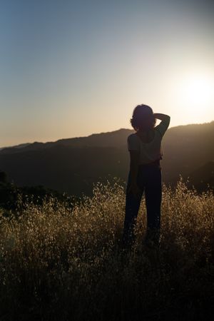 Back view silhouette of woman looking toward the sunset with her hand shielding her eyes