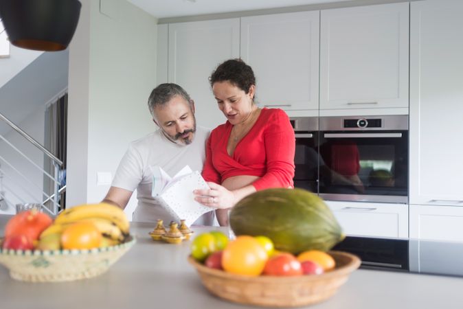 Smiling couple consulting recipe book in bright kitchen