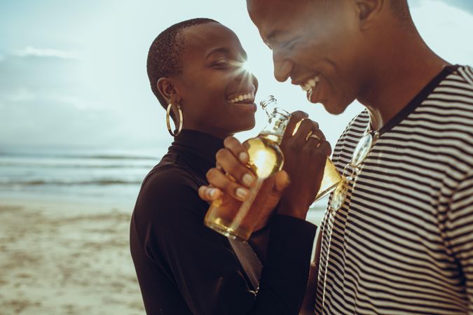 Smiling young man and woman standing at the beach having beers