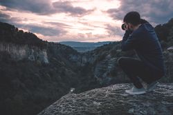 man with photo camera sitting on hill mountain with magnificent sunset