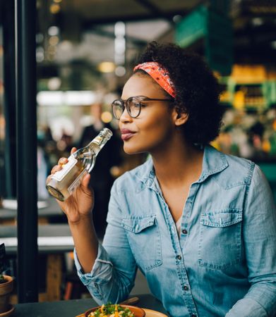 Woman about to take a sip out of a glass bottle in a cafe