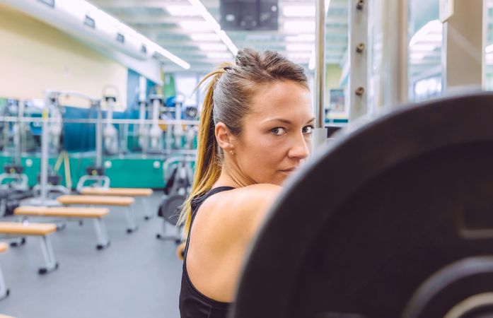 Focused woman standing at barbell looking at camera
