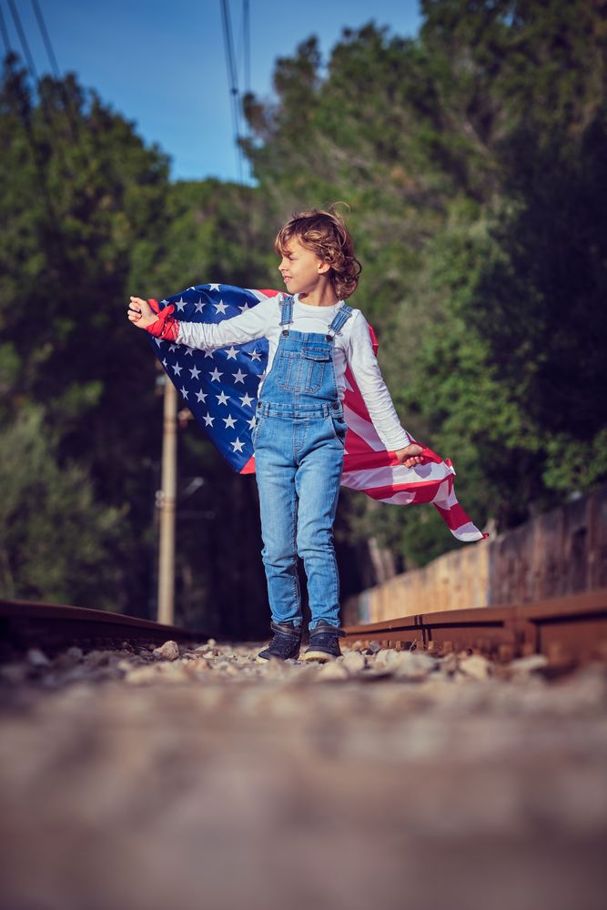 Child standing on railroad with flag of America in summer