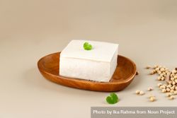 Tofu block on wooden plate with garnish and soybeans 4dORn5