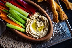 Creamy hummus dish served with chopped veggies and bread sticks on trey