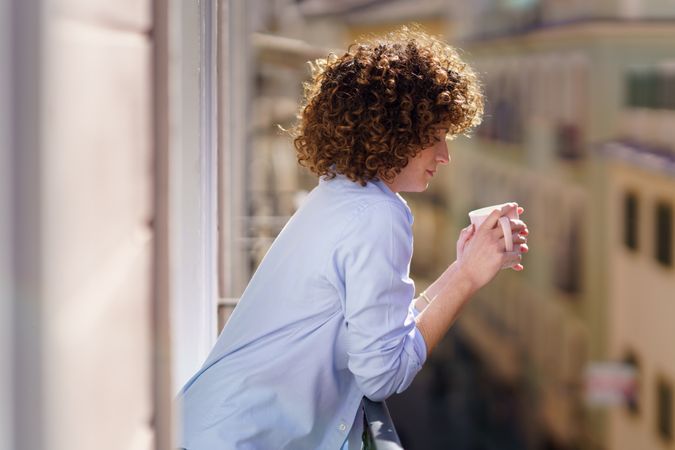 Contemplative woman with mug of coffee leaning on balcony