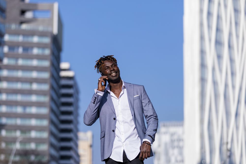 Smiling Black man wearing elegant clothes standing in the street while looking in the distance in sunny day