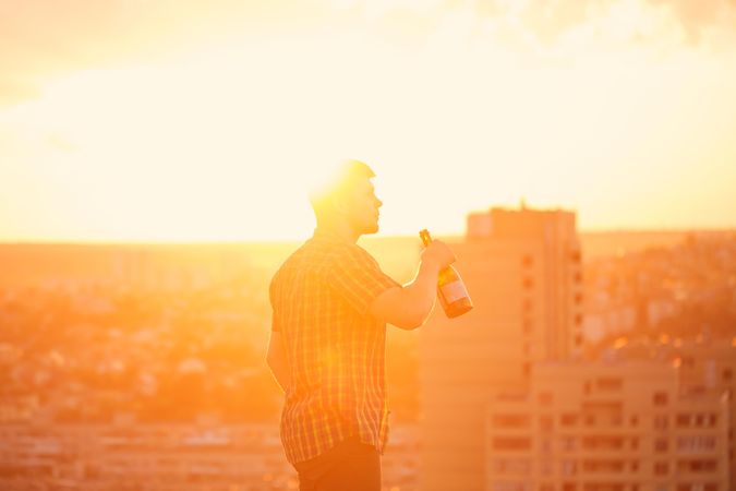 Man drinking from bottle of wine at sunset