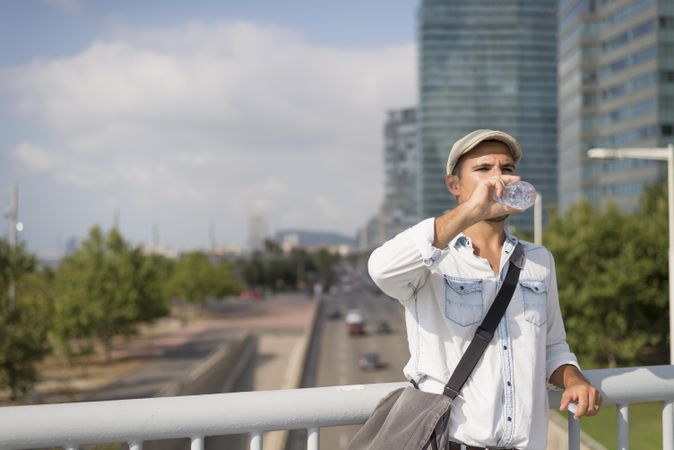 Relaxed male in denim with city in background drinking from water bottle, copy space