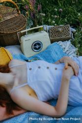 Woman laying on textile on green grass beside vintage radio 5aMvW5