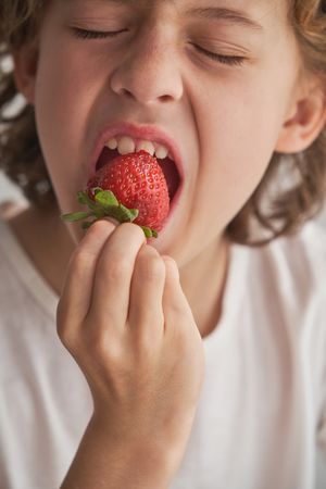 Crop positive boy biting strawberry
