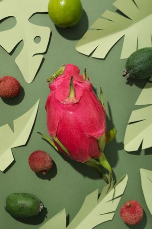 Tropical fruit and paper tropical leaves on green background, top view