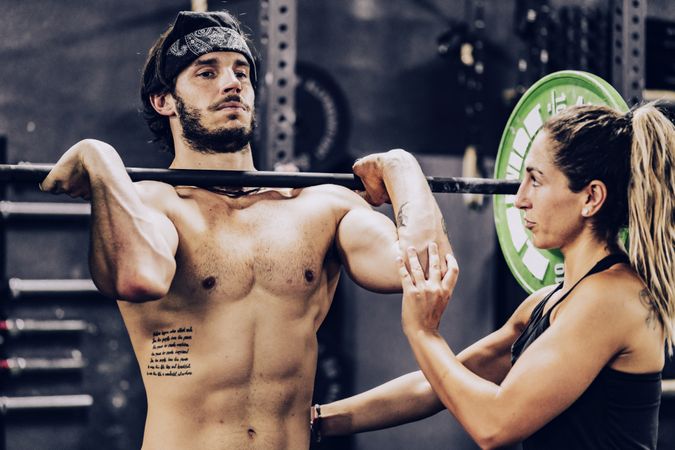 Muscular man lifting heavy weight in sport club and listening to personal trainer