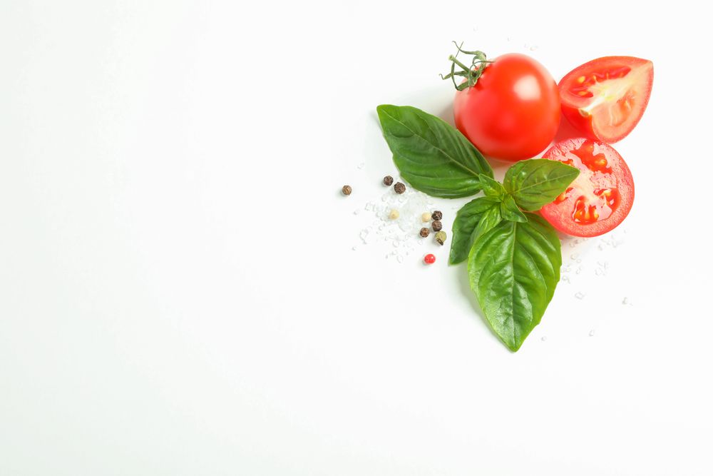 Fresh cherry tomatoes with basil and spices on plain background, space for text and top view. Ripe vegetables