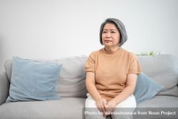 Single older Asian female sitting on couch at home 4BppP0