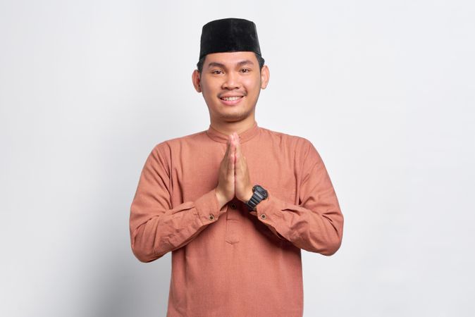 Smiling Muslim man in kufi head wear with his hands pressed together