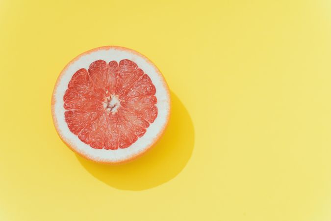 Red grapefruit slice on pastel yellow background