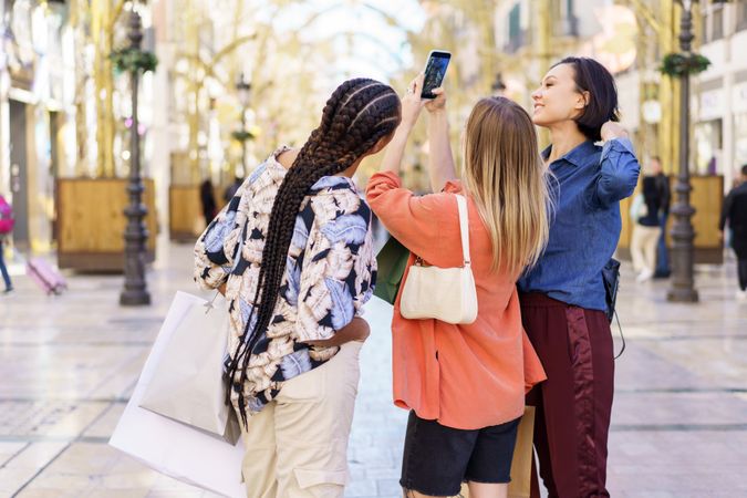 Three women looking up while taking picture in street with phone
