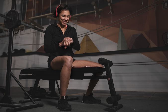 Athletic woman looking at watch on bench at gym