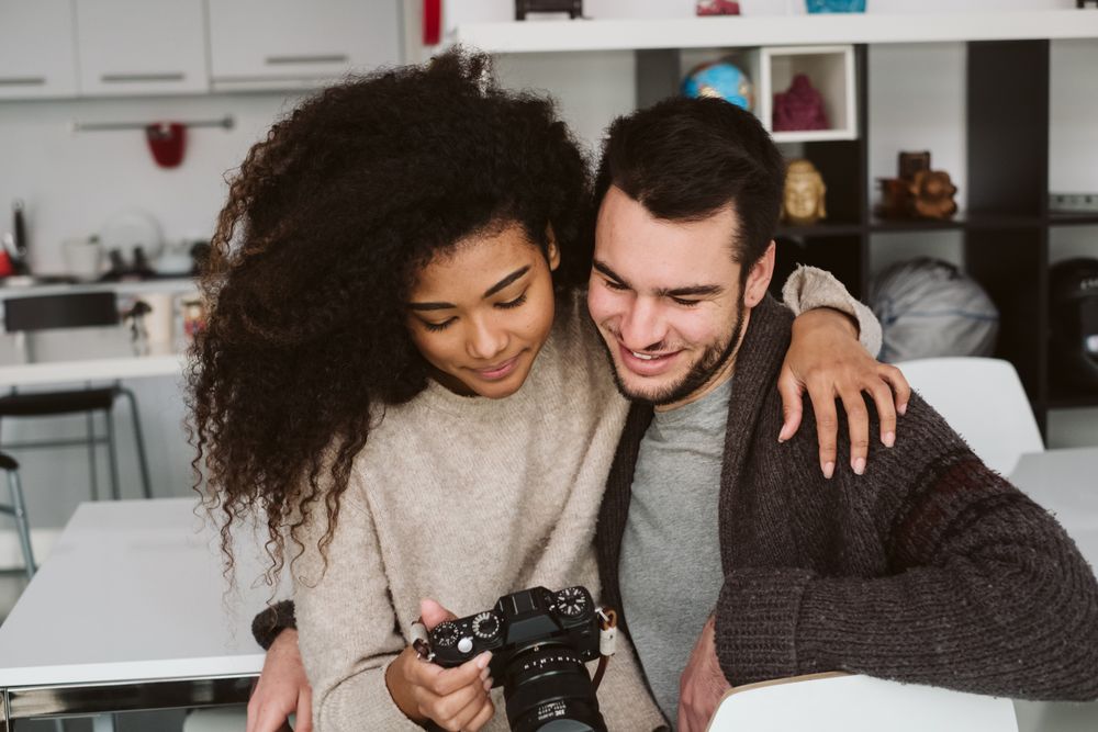 Multiracial couple looking at photo camera at home