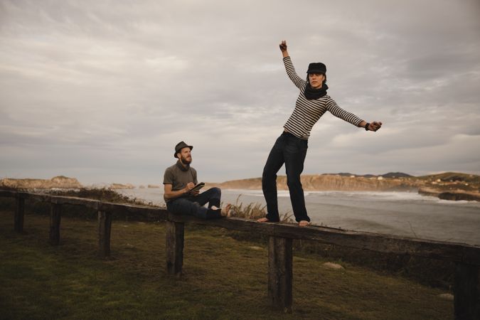 Couple holding hands and jumping on bench on shore near water