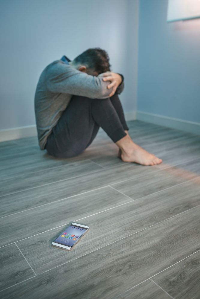 Man with problems sitting on the floor with mobile on the floor