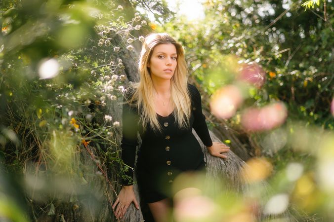 Pensive pregnant woman looking at camera while sitting in garden in sunny day